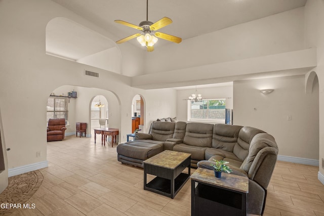 living area with arched walkways, a chandelier, a ceiling fan, baseboards, and high vaulted ceiling