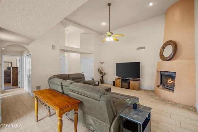 living area featuring a ceiling fan, a warm lit fireplace, arched walkways, high vaulted ceiling, and wood finish floors