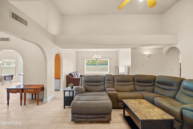 living room featuring arched walkways, a towering ceiling, ceiling fan, a chandelier, and baseboards