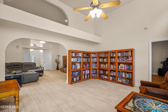 living area with arched walkways, high vaulted ceiling, ceiling fan, and baseboards