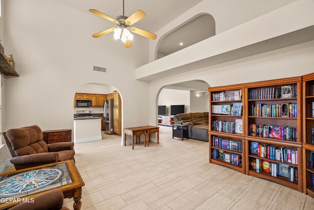 living room with arched walkways, ceiling fan, and a towering ceiling
