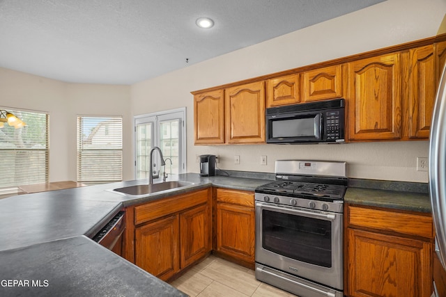 kitchen featuring stainless steel gas stove, black microwave, a sink, dark countertops, and brown cabinets