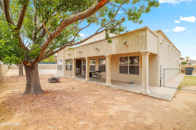 back of property with an outdoor fire pit, a gate, a patio area, stucco siding, and fence