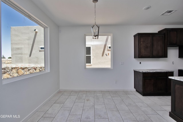 15341 Idea Ln, El Paso, TX 79938 - kitchen with dark brown cabinetry, hanging light fixtures, light stone counters, baseboards, and light tile patterned floors