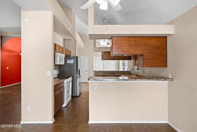 10740 White Sands Dr, El Paso, TX 79924 - kitchen with white appliances, a ceiling fan, brown cabinets, a peninsula, and baseboards