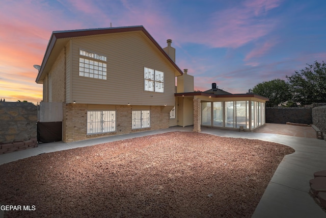 10740 White Sands Dr, El Paso, TX 79924 - back of house at dusk with a patio, a chimney, brick siding, and a sunroom