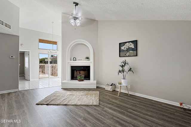 819 Los Surcos Rd, El Paso, TX 79907 - unfurnished living room featuring ceiling fan, high vaulted ceiling, wood finished floors, a textured ceiling, and a fireplace