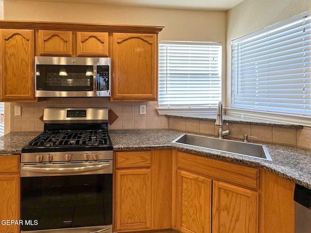 3081 Tierra Humeda Dr, El Paso, TX 79938 - kitchen with stainless steel appliances, a sink, tasteful backsplash, dark stone counters, and brown cabinetry