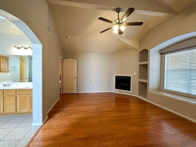 3081 Tierra Humeda Dr, El Paso, TX 79938 - unfurnished living room featuring vaulted ceiling, light wood-style flooring, a ceiling fan, built in features, and arched walkways