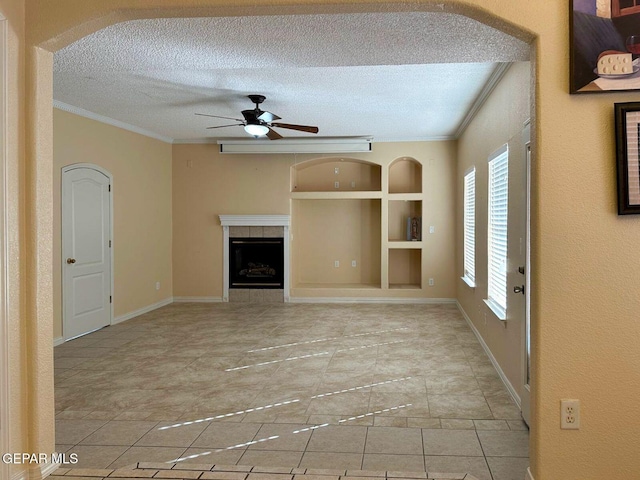 3081 Tierra Humeda Dr, El Paso, TX 79938 - unfurnished living room with crown molding, a textured ceiling, a ceiling fan, built in shelves, and a tiled fireplace