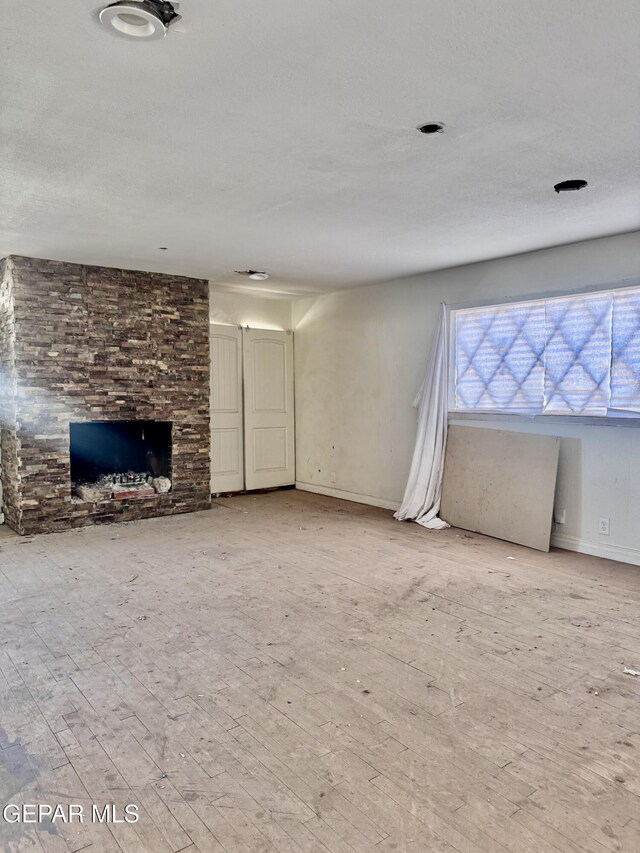4500 Frankfort Ave, El Paso, TX 79903 - unfurnished living room with wood finished floors, a stone fireplace, and baseboards