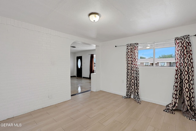 5713 Sanders Ave, El Paso, TX 79924 - unfurnished room featuring arched walkways, light wood-style floors, a textured ceiling, baseboards, and brick wall