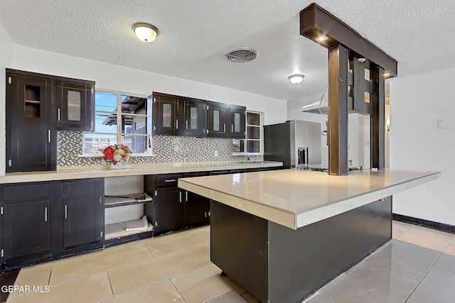 5713 Sanders Ave, El Paso, TX 79924 - kitchen featuring stainless steel fridge, backsplash, light countertops, light tile patterned flooring, and a textured ceiling
