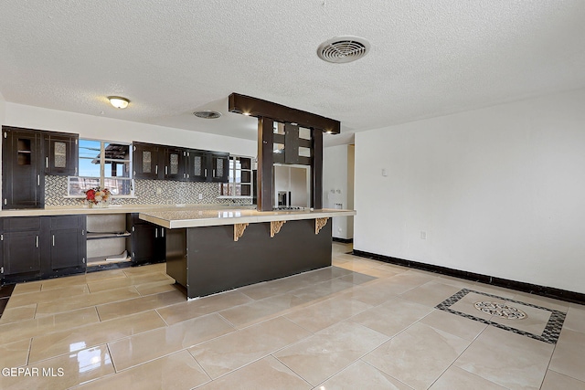 5713 Sanders Ave, El Paso, TX 79924 - kitchen with light countertops, a breakfast bar, glass insert cabinets, backsplash, and light tile patterned flooring