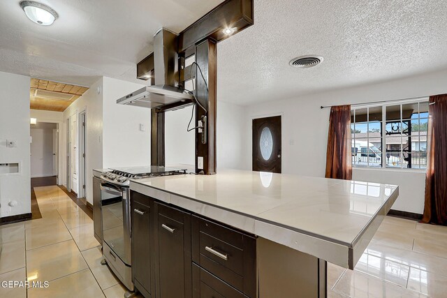 5713 Sanders Ave, El Paso, TX 79924 - kitchen with gas stove, light tile patterned floors, baseboards, dark brown cabinetry, and wall chimney exhaust hood