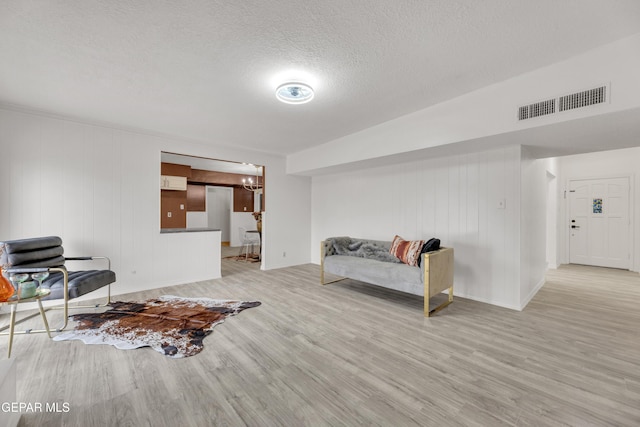 living area featuring light wood-style flooring, a textured ceiling, and baseboards