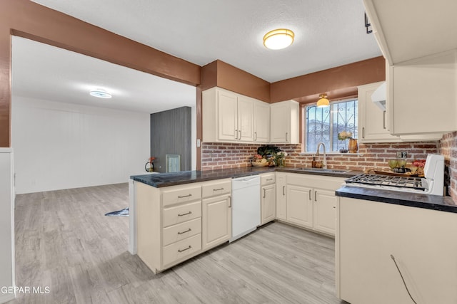 kitchen with dishwasher, a sink, dark countertops, light wood-style flooring, and a textured ceiling