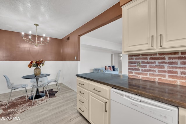 kitchen featuring dishwasher, dark countertops, a chandelier, light wood finished floors, and wainscoting