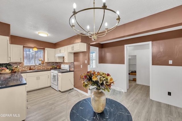 kitchen with white gas stove, a sink, dark countertops, a chandelier, and light wood finished floors