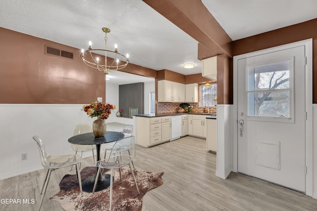 kitchen with dishwasher, a chandelier, light wood finished floors, a sink, and dark countertops