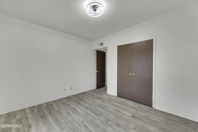 unfurnished bedroom with a textured ceiling, light wood-type flooring, and baseboards
