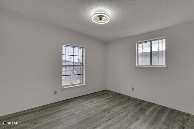 empty room featuring plenty of natural light, wood finished floors, a textured ceiling, and baseboards