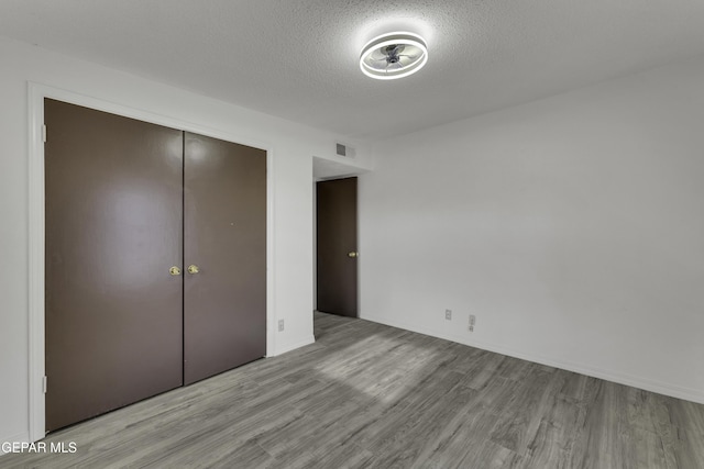 unfurnished bedroom with wood finished floors, a textured ceiling, and a closet