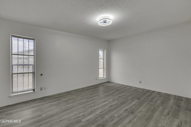 spare room featuring a textured ceiling, wood finished floors, healthy amount of natural light, and baseboards