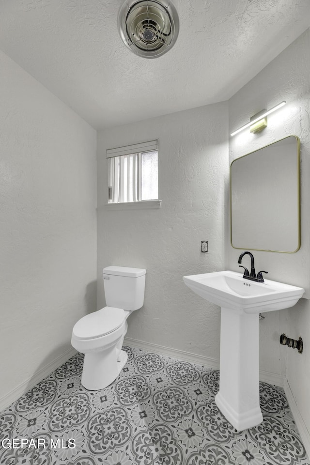 bathroom with toilet, a textured ceiling, baseboards, and tile patterned flooring