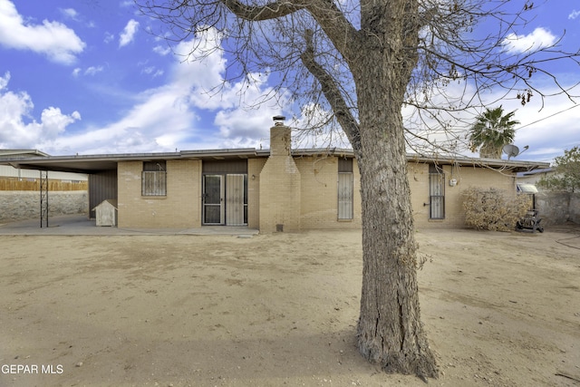 back of property featuring a chimney, brick siding, and an attached carport