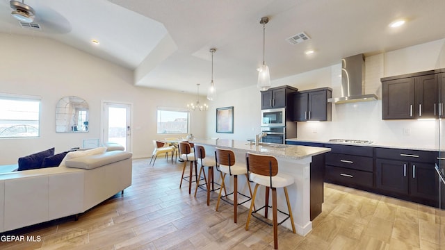 569 Logwood Ave, Canutillo, TX 79835 - kitchen featuring appliances with stainless steel finishes, wall chimney range hood, a kitchen bar, open floor plan, and light wood-type flooring