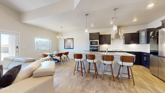 569 Logwood Ave, Canutillo, TX 79835 - kitchen featuring stainless steel appliances, wall chimney range hood, open floor plan, a breakfast bar area, and a chandelier