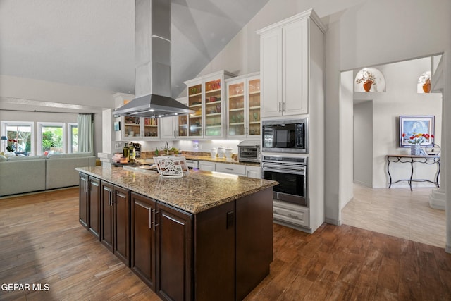 12081 E Paseo De Amor Ln E, El Paso, TX 79936 - kitchen featuring stainless steel appliances, island range hood, white cabinetry, dark brown cabinets, and light stone countertops