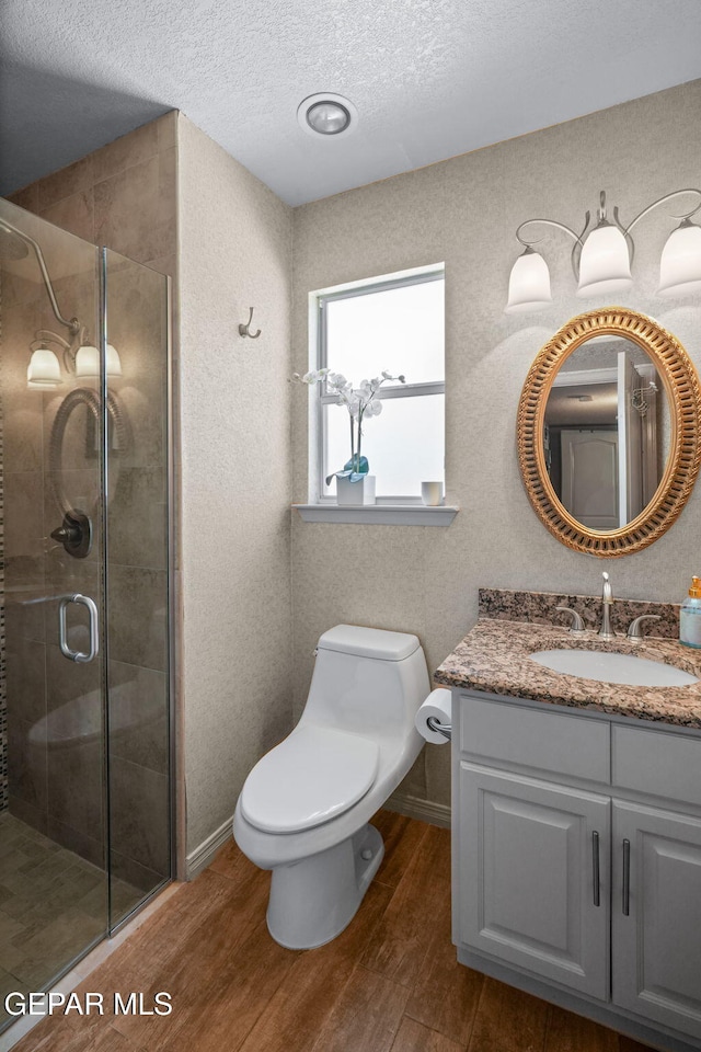 12081 E Paseo De Amor Ln E, El Paso, TX 79936 - bathroom featuring wood finished floors, a shower stall, vanity, toilet, and a textured ceiling