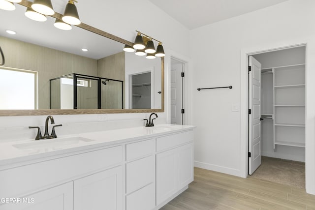 10700 Elise St, El Paso, TX 79924 - bathroom featuring a walk in closet, a shower stall, wood finished floors, double vanity, and baseboards