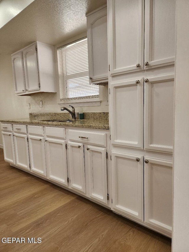 301 Bandolina Dr, Socorro, TX 79927 - kitchen featuring light wood finished floors, white cabinets, a sink, light stone counters, and a textured ceiling
