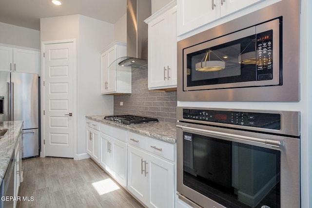7389 Cimarron Gap Dr, El Paso, TX 79911 - kitchen featuring stainless steel appliances, wall chimney exhaust hood, light stone counters, white cabinetry, and tasteful backsplash