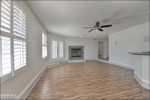4372 Loma De Oro Dr, El Paso, TX 79934 - unfurnished living room with a ceiling fan, wood finished floors, a textured ceiling, a stone fireplace, and baseboards