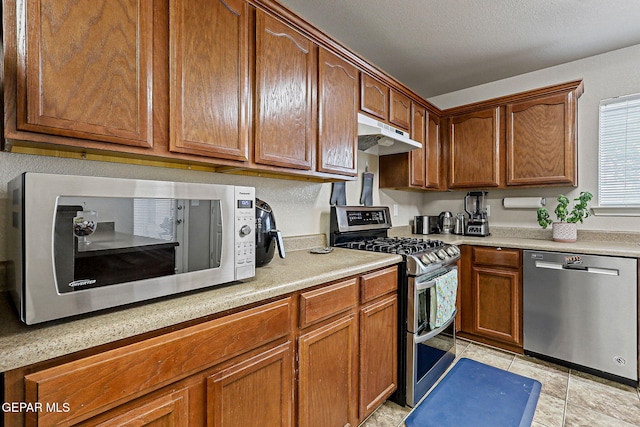 14181 Rudy Valdez Dr, El Paso, TX 79938 - kitchen featuring stainless steel appliances, under cabinet range hood, light countertops, and brown cabinetry