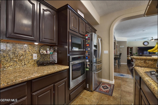 1337 Emerald Gate Ln, El Paso, TX 79936 - kitchen with stainless steel appliances, backsplash, dark brown cabinetry, arched walkways, and a textured ceiling