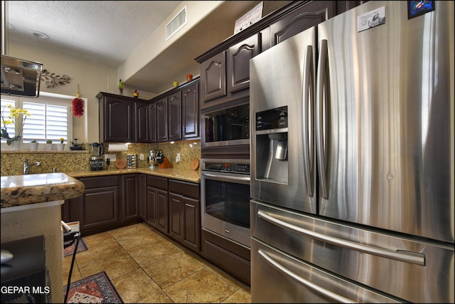 1337 Emerald Gate Ln, El Paso, TX 79936 - kitchen with appliances with stainless steel finishes, backsplash, dark brown cabinetry, a textured ceiling, and light tile patterned floors