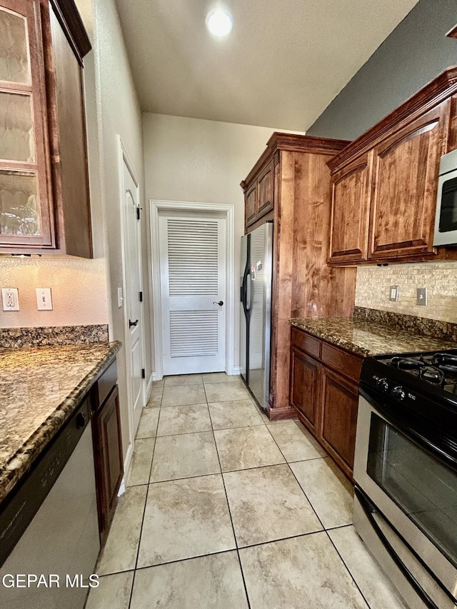11609 Saint Thomas Way, El Paso, TX 79936 - kitchen featuring appliances with stainless steel finishes, tasteful backsplash, glass insert cabinets, light tile patterned flooring, and dark stone countertops