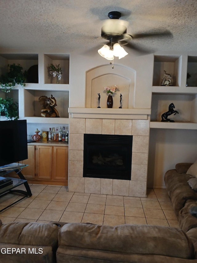 405 Santorini Ct, Socorro, TX 79927 - living room featuring a textured ceiling, light tile patterned floors, a tiled fireplace, a ceiling fan, and built in shelves