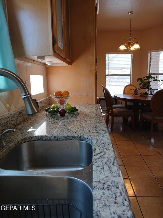 405 Santorini Ct, Socorro, TX 79927 - kitchen with a chandelier, light tile patterned floors, brown cabinetry, pendant lighting, and light stone countertops