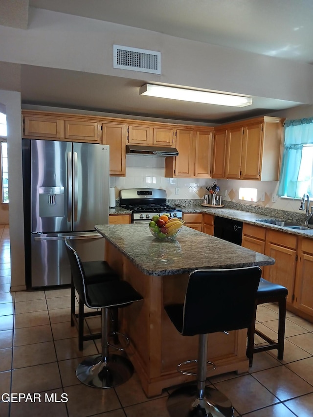 405 Santorini Ct, Socorro, TX 79927 - kitchen with appliances with stainless steel finishes, under cabinet range hood, light tile patterned floors, a kitchen island, and a kitchen bar