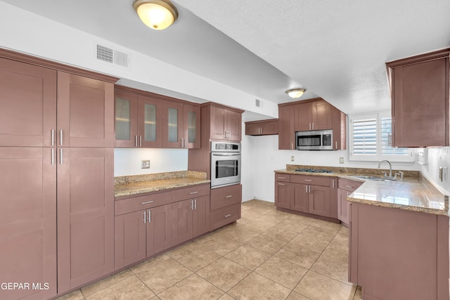 7461 Plaza Redonda Dr, El Paso, TX 79912 - kitchen featuring stainless steel appliances, a sink, light stone countertops, light tile patterned floors, and glass insert cabinets