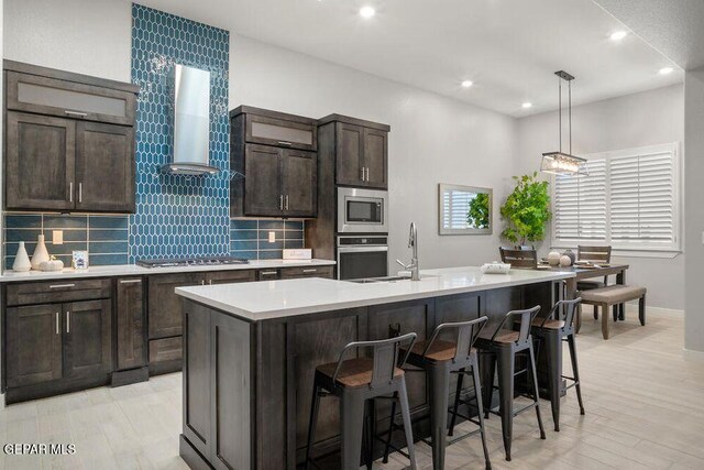 2212 Mike Price Dr, El Paso, TX 79938 - kitchen featuring stainless steel appliances, wall chimney range hood, light countertops, an island with sink, and tasteful backsplash