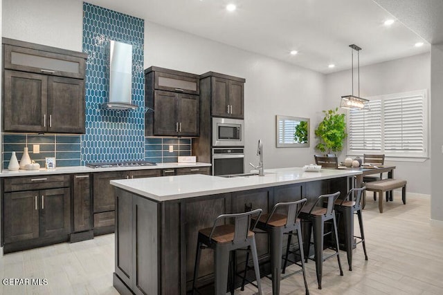 2228 Mike Price Dr, El Paso, TX 79938 - kitchen featuring stainless steel appliances, wall chimney range hood, light countertops, an island with sink, and tasteful backsplash