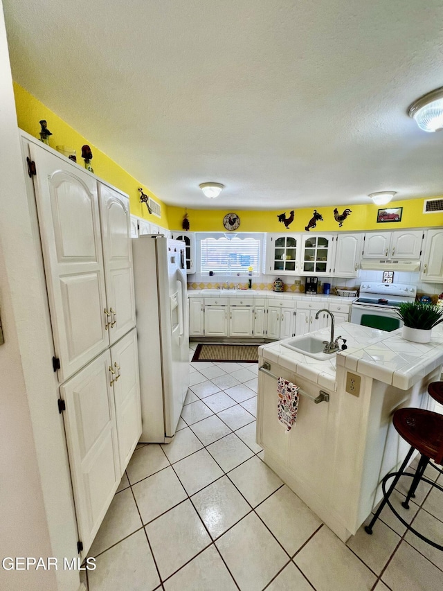 16899 Old Butterfield Trl, El Paso, TX 79938 - kitchen with white appliances, tile countertops, glass insert cabinets, a textured ceiling, and light tile patterned flooring