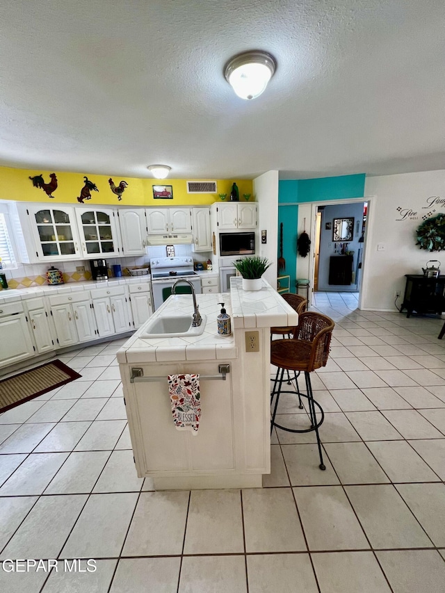 16899 Old Butterfield Trl, El Paso, TX 79938 - kitchen with tile counters, built in microwave, electric stove, a center island with sink, and white cabinetry
